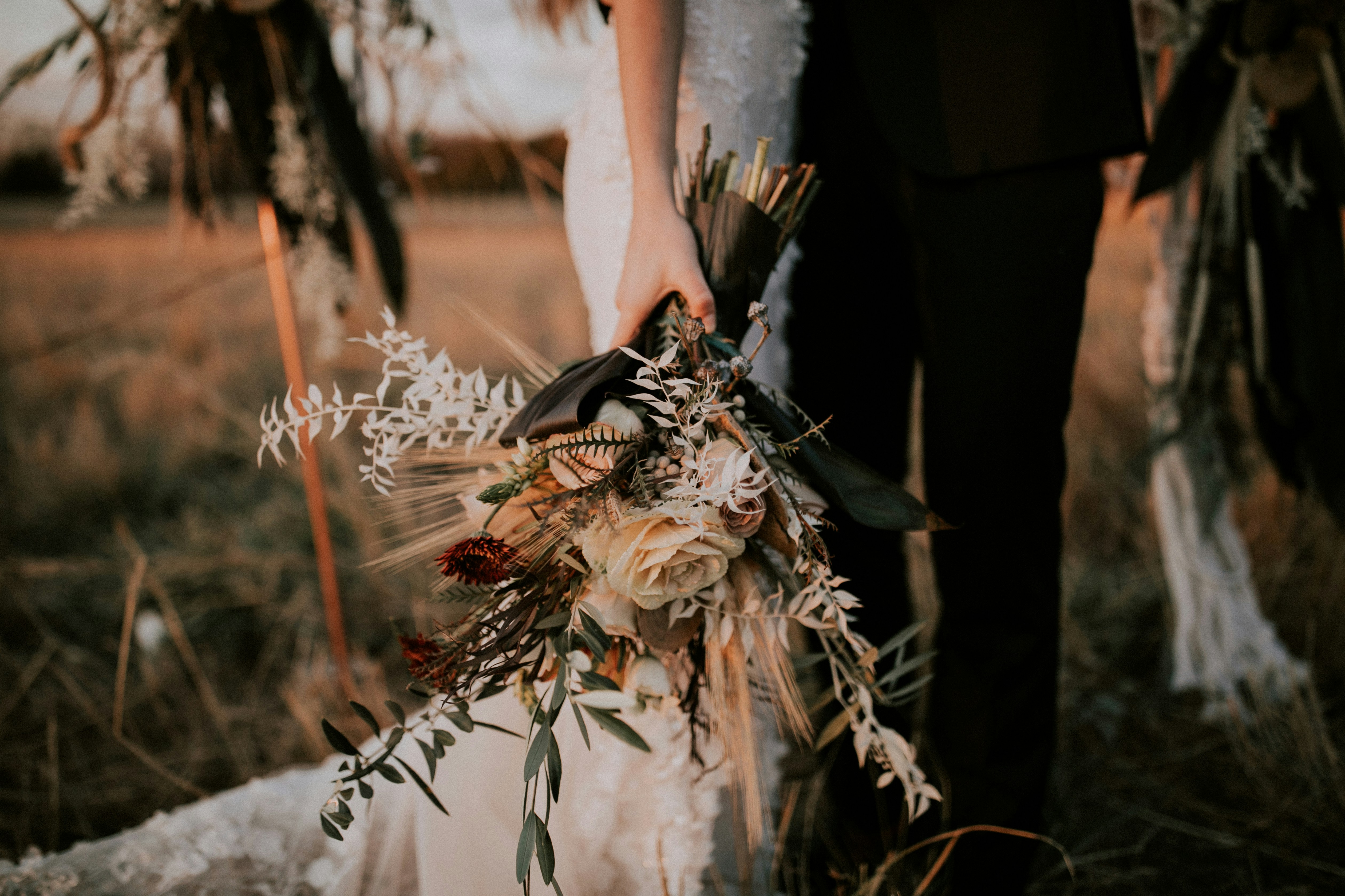 A couple at their outdoor ceremony, the bride holding a bouquet of dried roses, wheat and eucalyptus in warm evening light